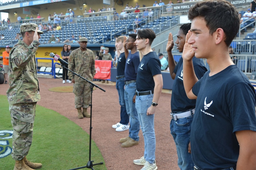 Young people in T-shirts face a person in uniform and raise their right hands.