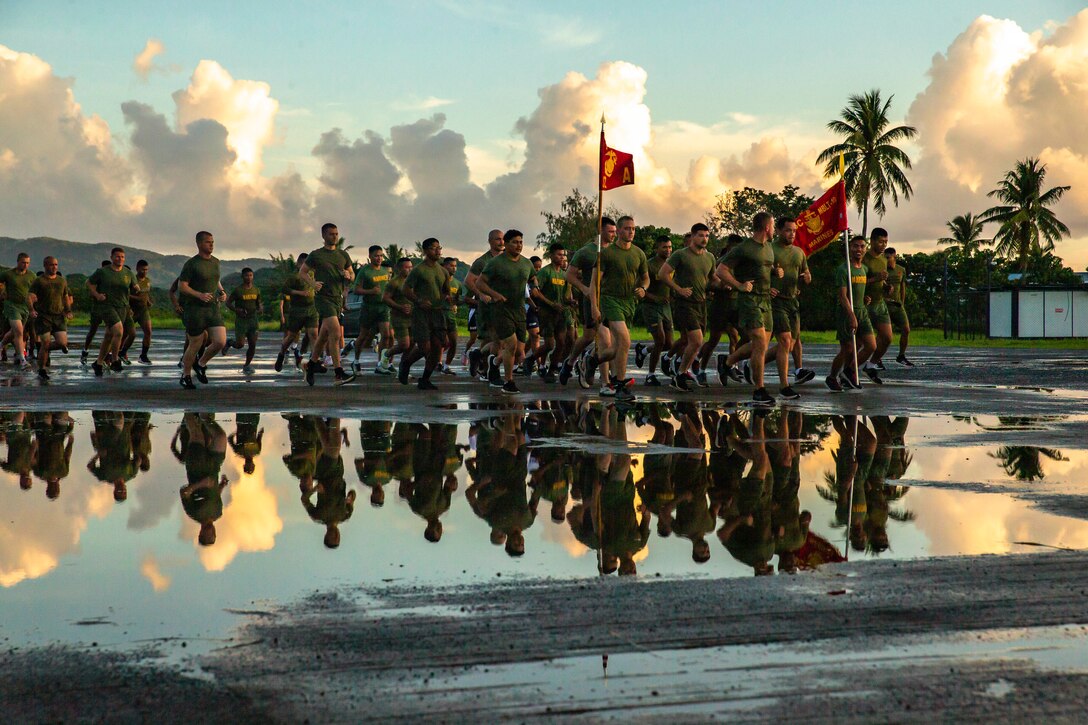 A group of Marines run together as seen through the reflection of a puddle.