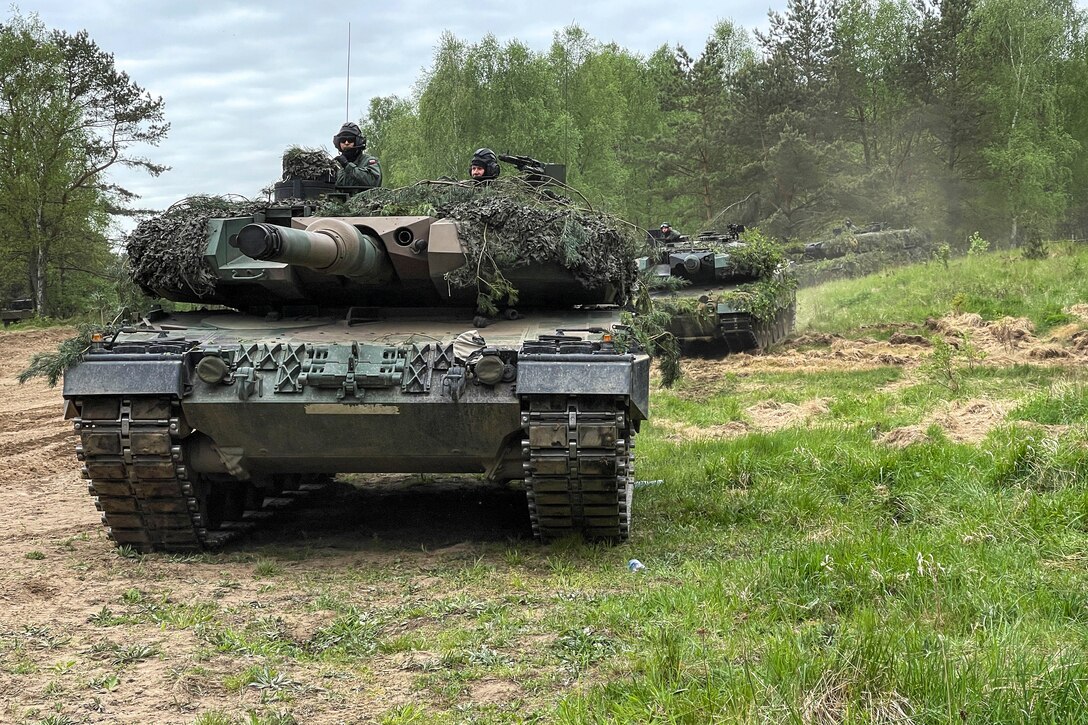 Tanks draped with tree branches operate a forested area.