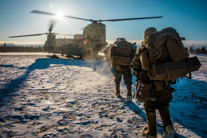 Uniformed personnel march through the snow toward a helicopter.