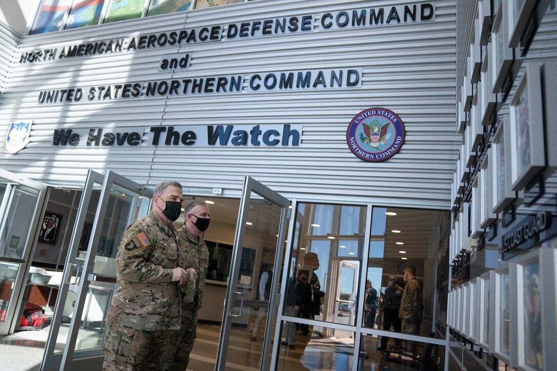 Two men in uniform stand in front of a large sign that says "North American Aerospace Defense Command and United States Northern Command. We have the watch."