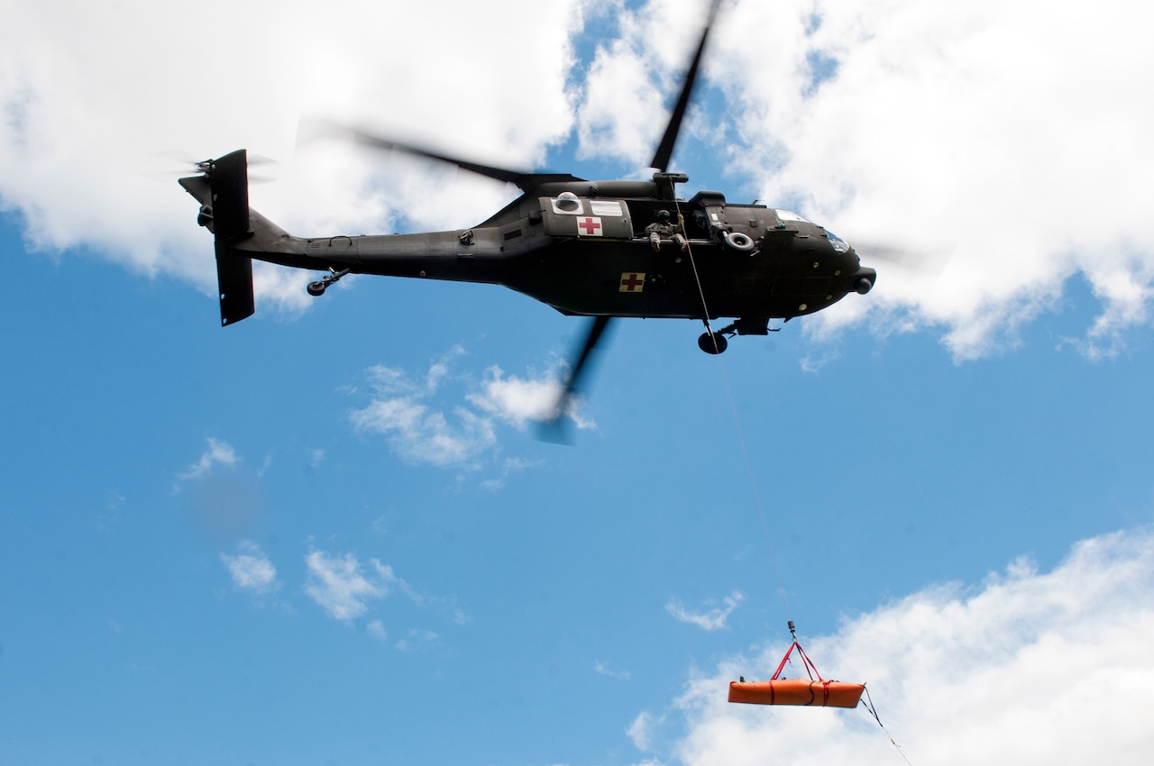 A stretcher hangs beneath a hovering helicopter.