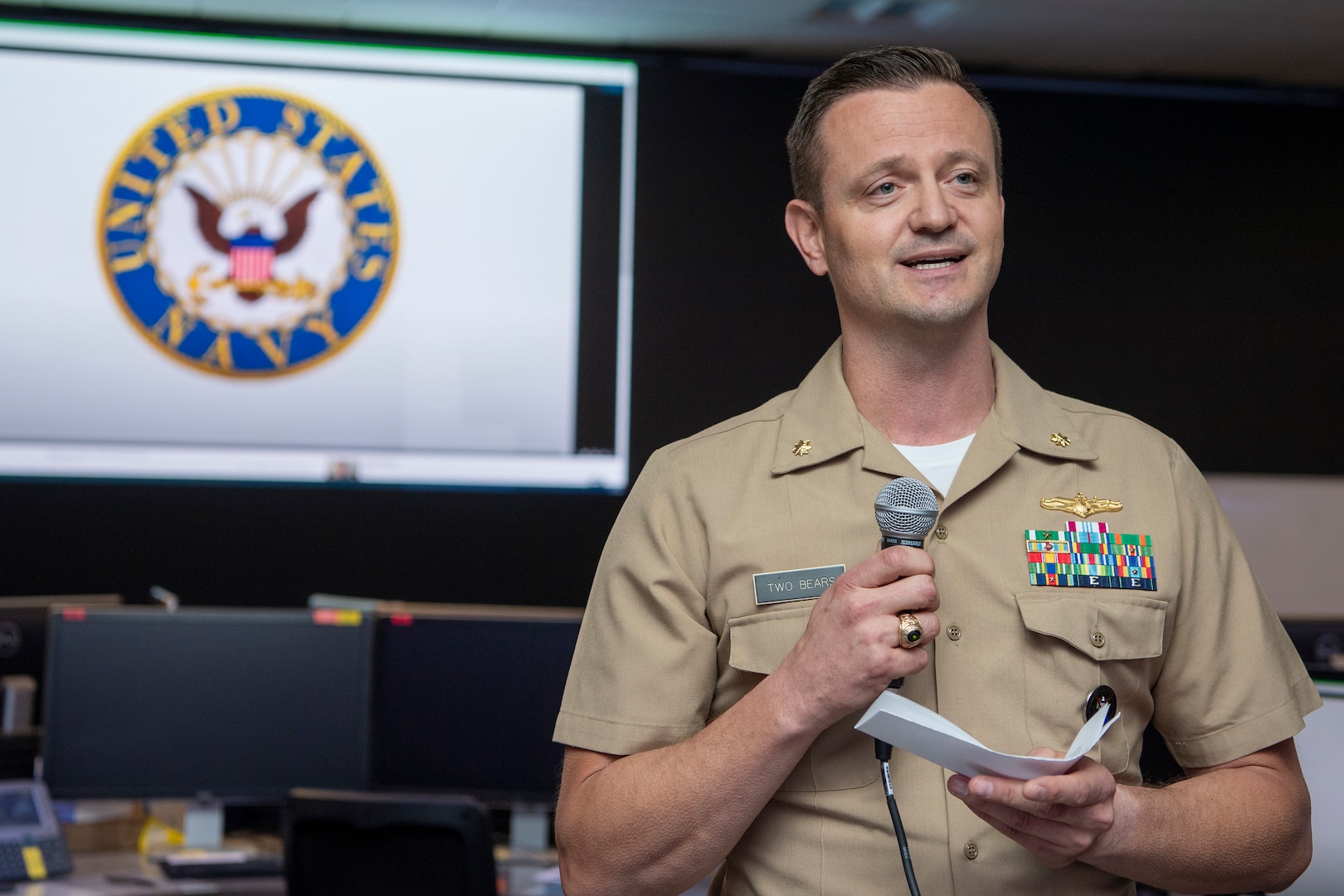 Navy man in uniform holds microphone and reads remarks