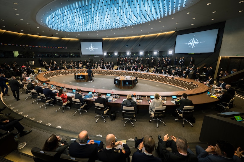 Numerous people gather in a room around a circular table