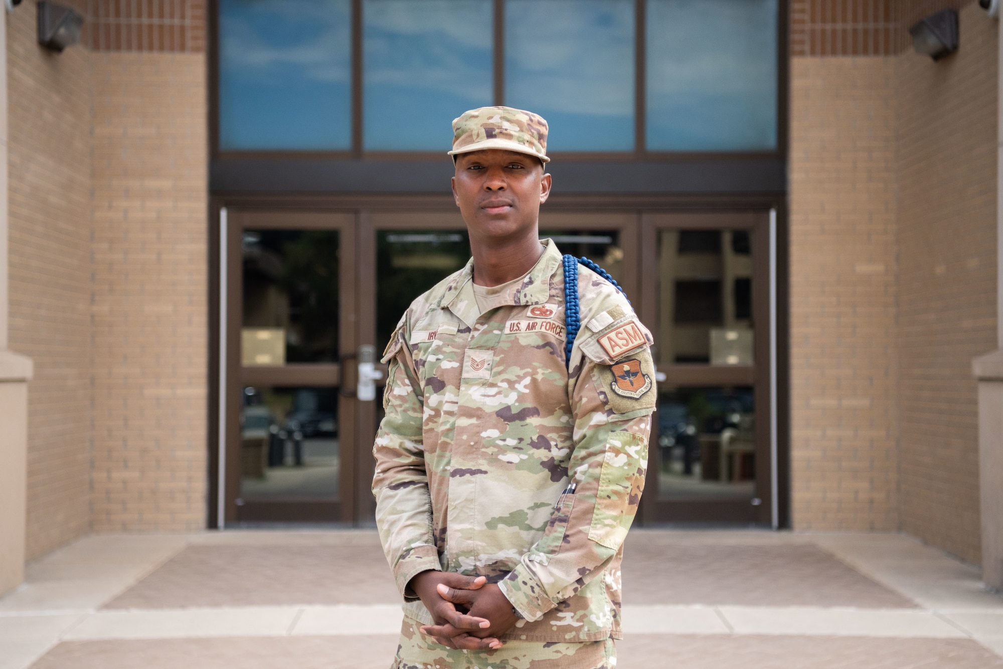 Man poses in front of building with his hands interlocked in front of his body.