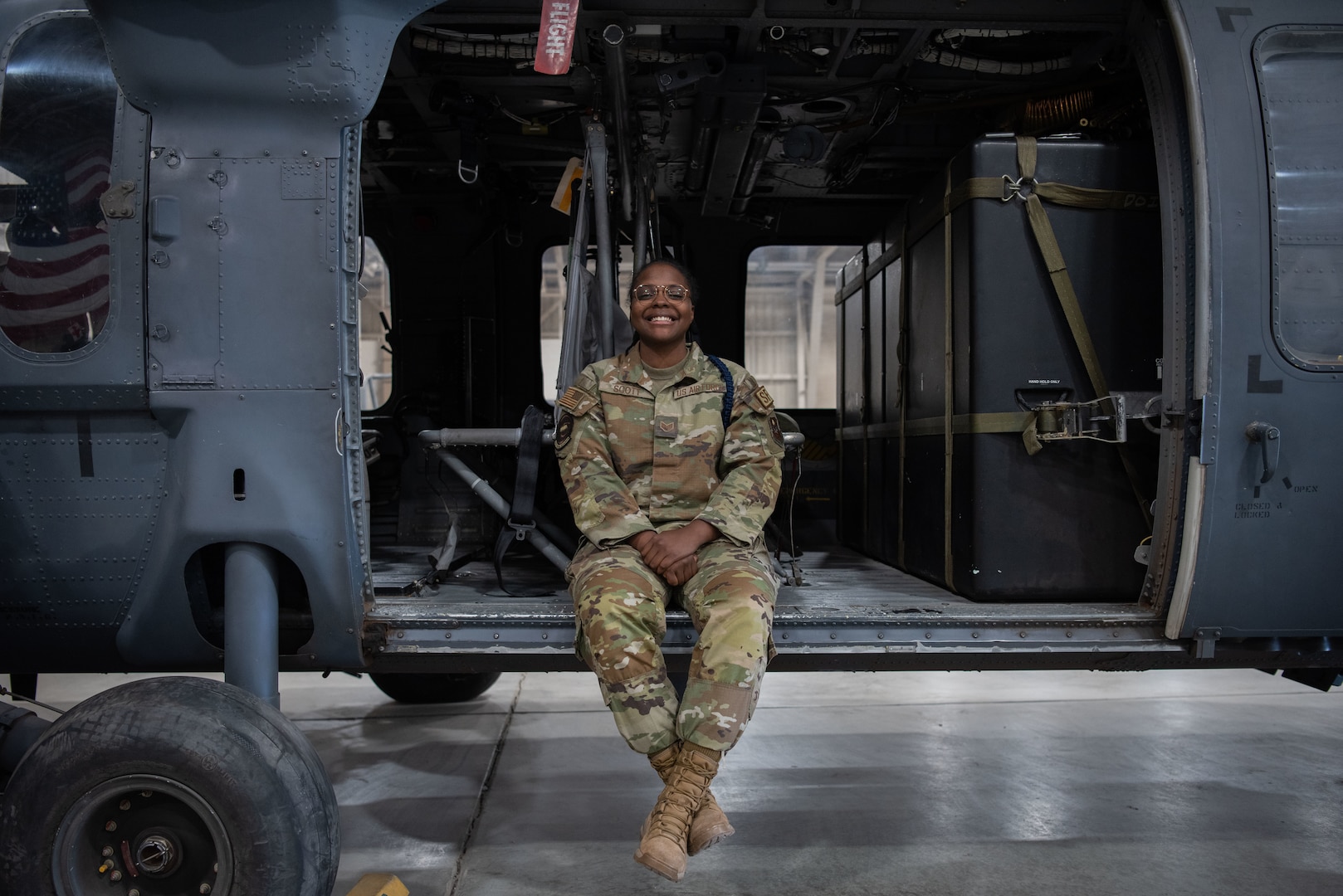 Woman is sitting in helicopter with her legs crossed, left foot on top of the right. She is smiling at the camera with her hands interlocked in front of her.