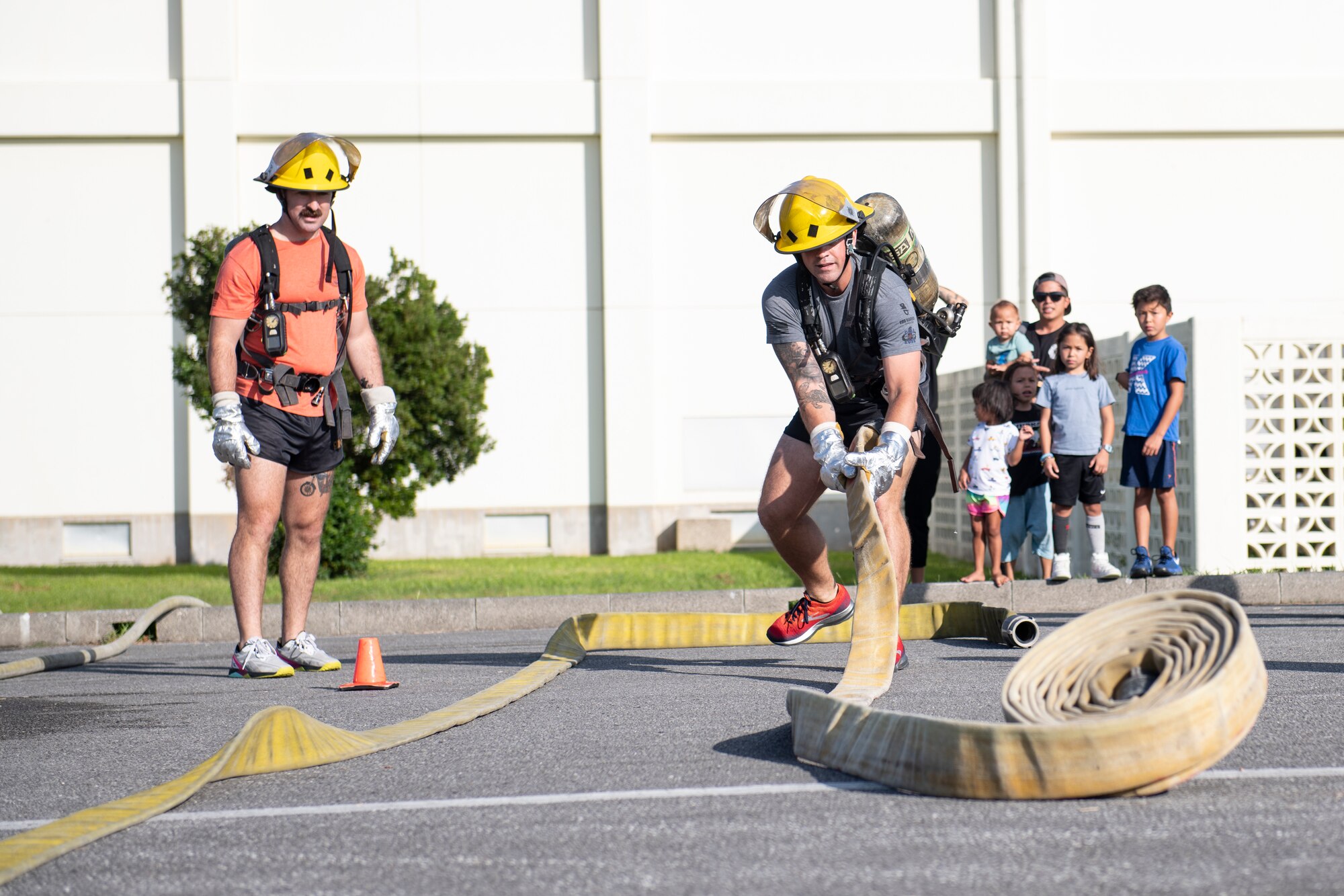 Tech. Sgt. Jordan Oswald, 18th Civil Engineer Squadron explosive ordnance disposal team leader, unfurls a hose at the fire muster challenge during National Fire Prevention Week at Kadena Air Base, Japan, Oct. 6, 2022. The relay event gave teams of four the opportunity to compete for best time while conquering firefighter training-related obstacles. (U.S. Air Force photo by Senior Airman Jessi Roth)