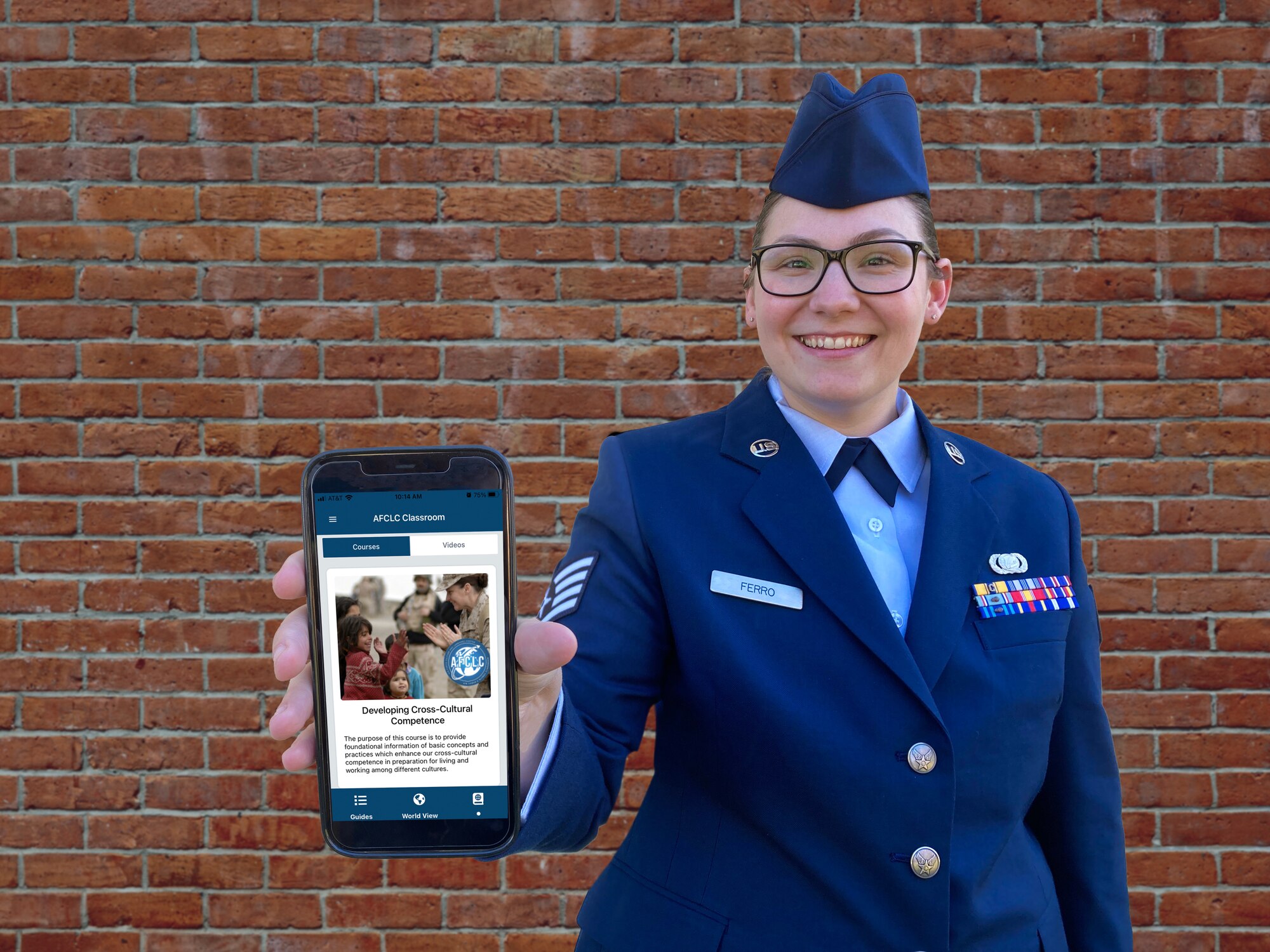 Airman standing in front of a brick wall showing Culture Guide app course on phone