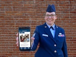 Airman standing in front of a brick wall showing Culture Guide app course on phone