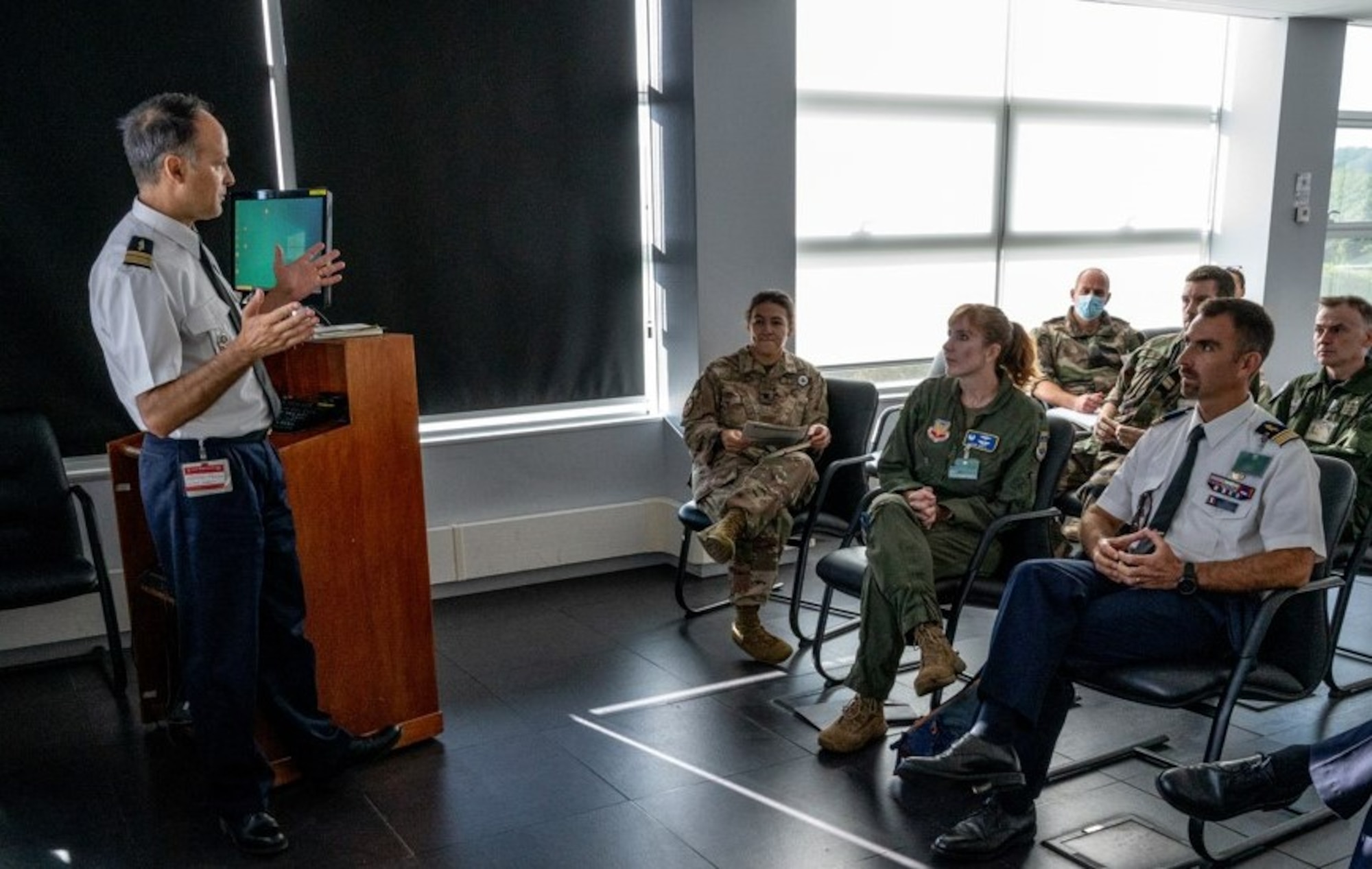 photo of  French air force member standing briefing a group of US and French military personnel sitting in chairs