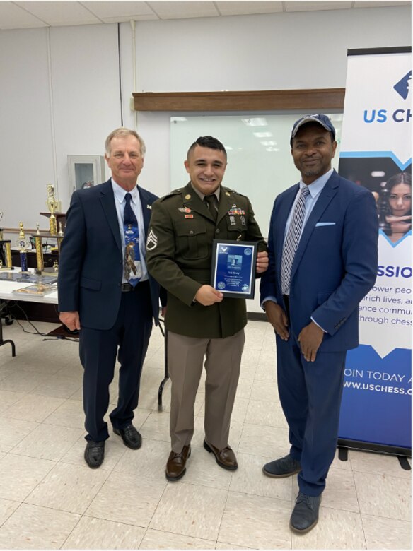 Solder stands in between two civilians holding award.