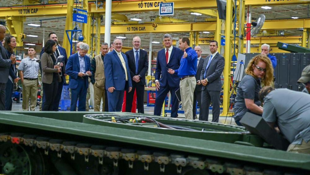 Several people wearing business attire gather around a large piece of equipment inside a factory.