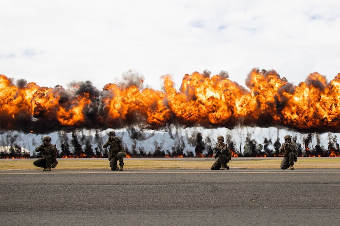 U.S. Marines with 3d Littoral Combat Team, 3rd Marine Littoral Regiment, take a knee in front of an explosives display, nicknamed the "Wall of Fire," during a Joint Air-Ground Task Force Demonstration as part of the 2022 Kaneohe Bay Air Show, Marine Corps Air Station Kaneohe Bay, Marine Corps Base Hawaii, Aug. 13, 2022. The air show provided an opportunity to showcase the aircraft, equipment and capabilities of the armed forces to the local community. The Kaneohe Bay Air Show, which contained aerial performances, static displays, demonstrations and vendors, was designed to celebrate MCBH’s longstanding relationship with the local community. (U.S. Marine Corps photo by Cpl. Brandon Aultman)
