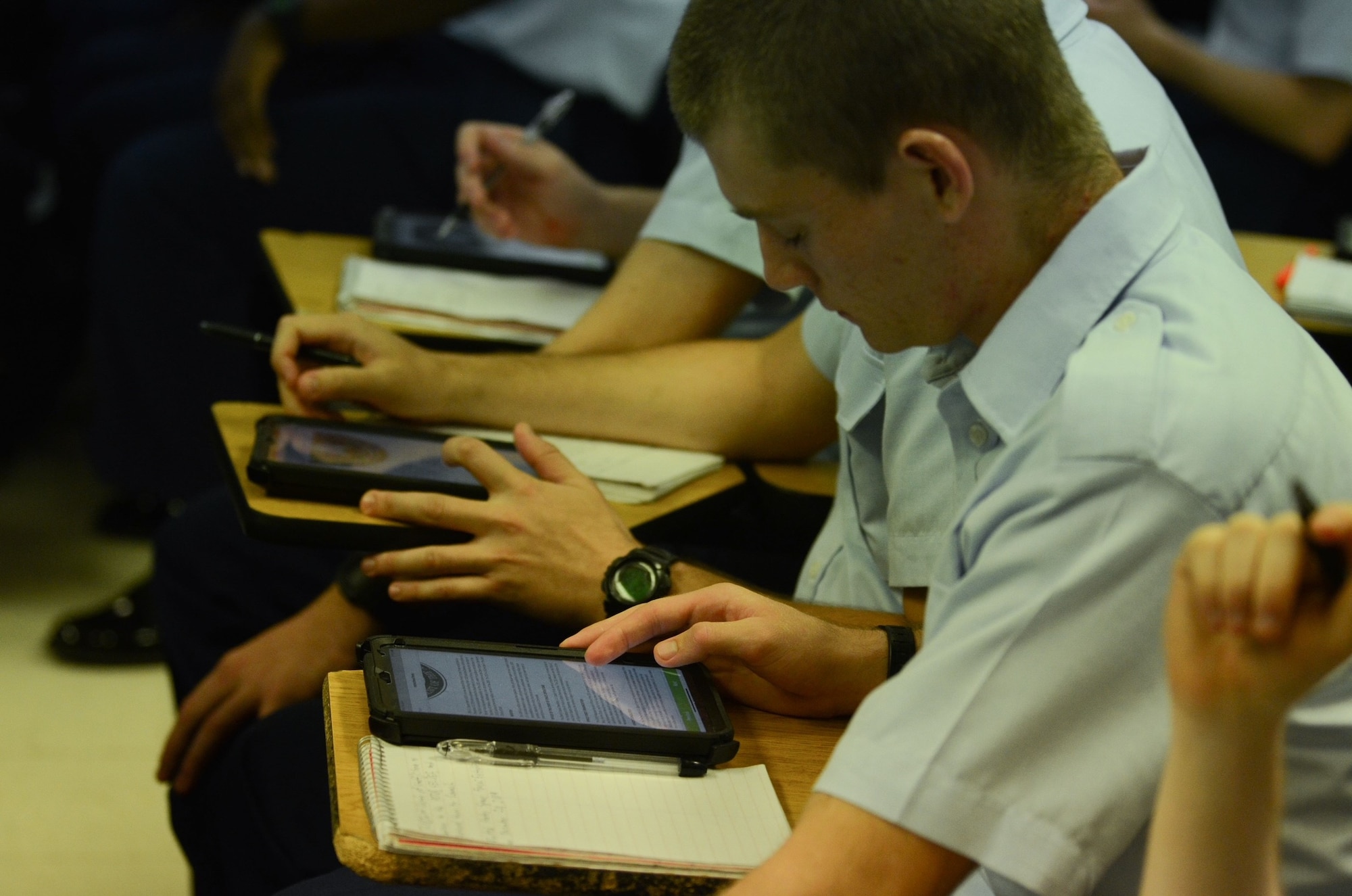 Student looking down at an iPad while sitting at a desk.