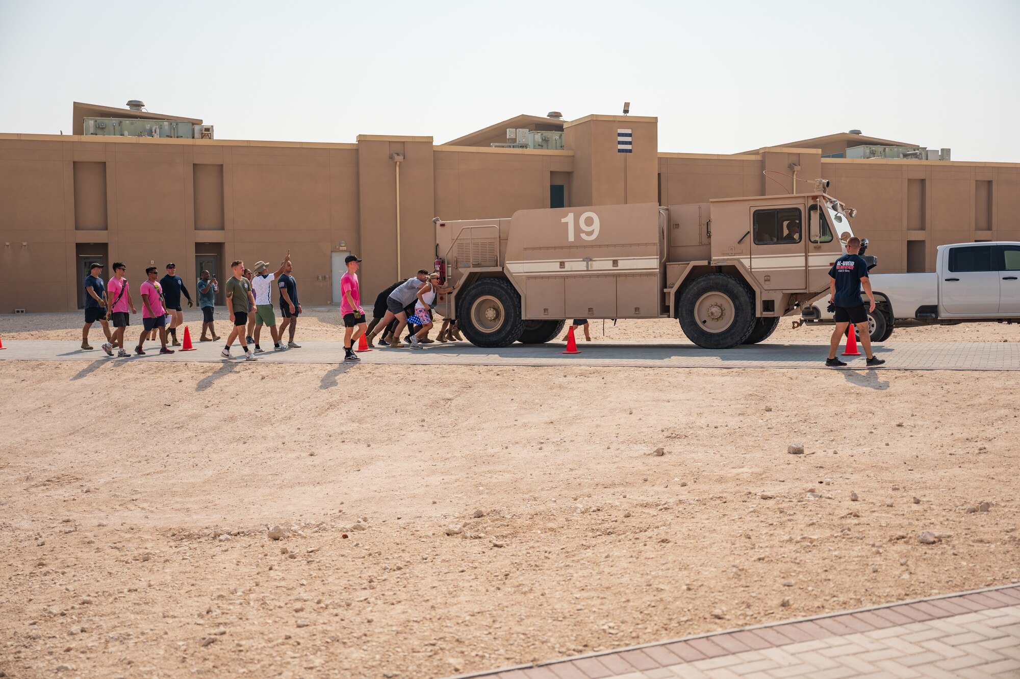 U.S. Air Force firefighters assigned to the 379th Expeditionary Civil Engineering Squadron and Airmen push a fire truck at the fire rodeo exercise Oct 15, 2022 at Al Udeid Air Base, Qatar. During fire safety week the firefighters conducted the fire rodeo where they hosted an open competition featuring elements of physical prowess needed to perform the lifesaving skills associated with their job. (U.S. Air Force photo by Staff Sgt. Dana Tourtellotte)