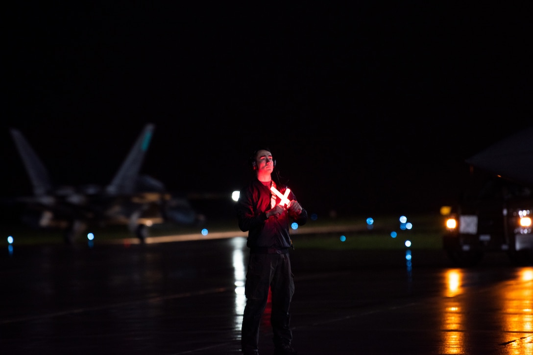 A man standing at night crosses two glowing signal sticks.