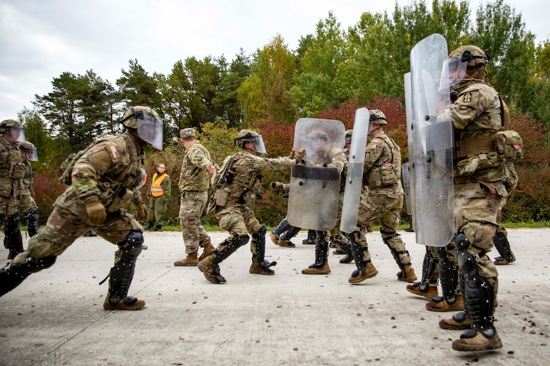 Soldiers wearing masks and carrying shields confront each other.