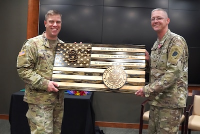 Lt. Col. Joseph Harris, the Recruiting and Retention Battalion commander, presents a wooden flag to Sgt. 1st Class Robert Gasen, of Girard Illinois, during his retirement ceremony at Camp Lincoln in Springfield, Illinois, October 13.