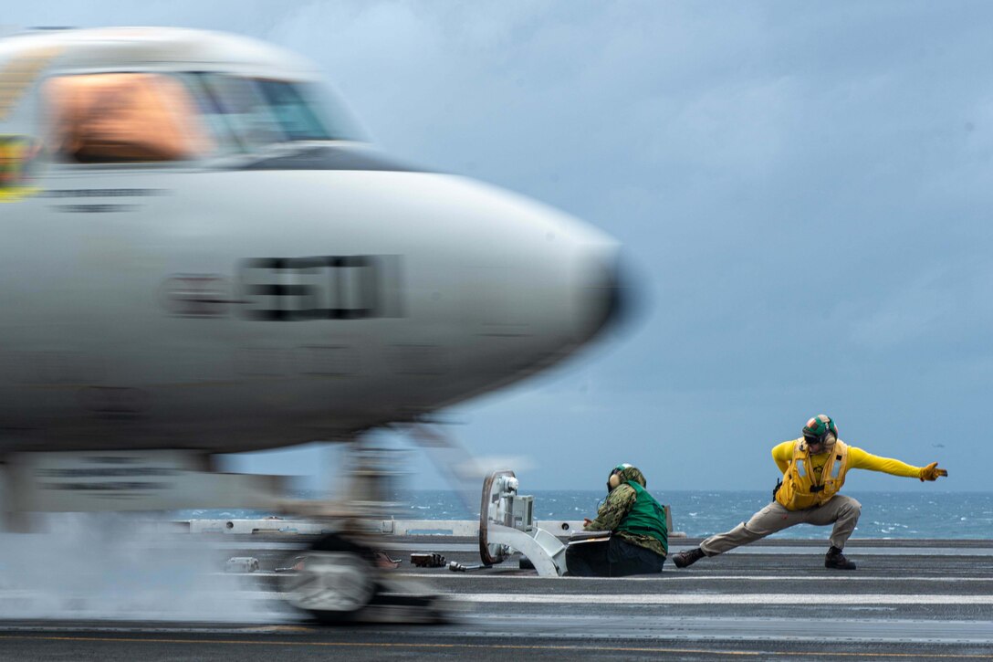 A sailor signals for an aircraft to take off from a ship.