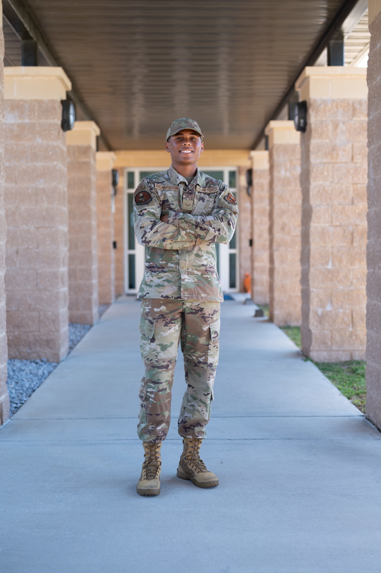 An Airman poses for a portrait on the walkway leading into a building.
