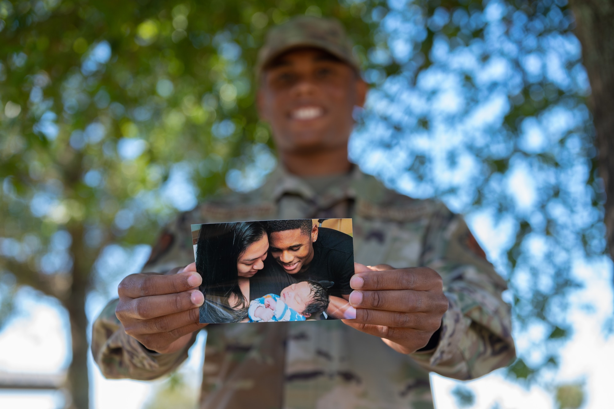 An Airman holds out a photo of his wife, his baby and himself.
