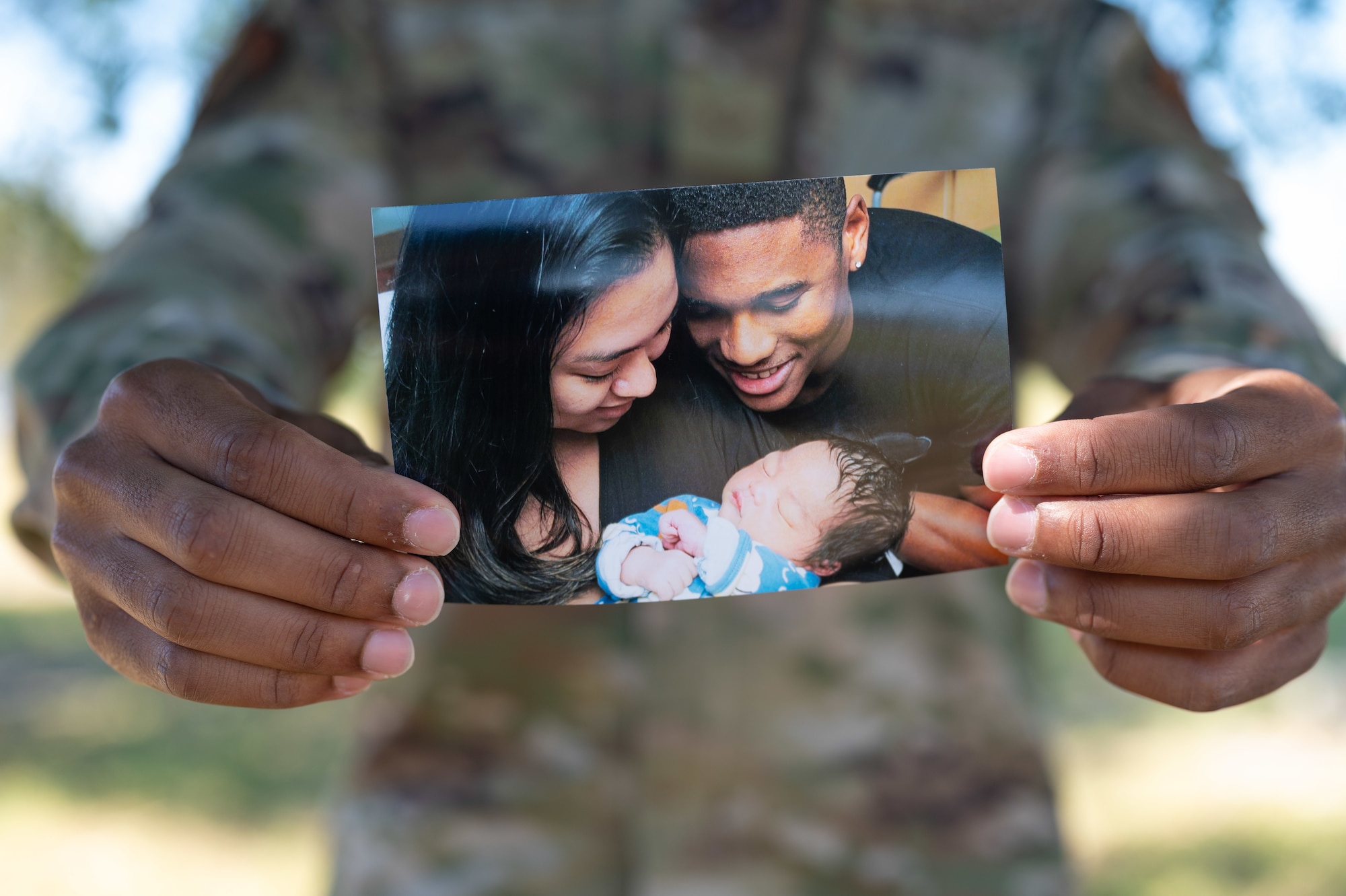 An Airman holds out a photo of his wife, his baby and himself.