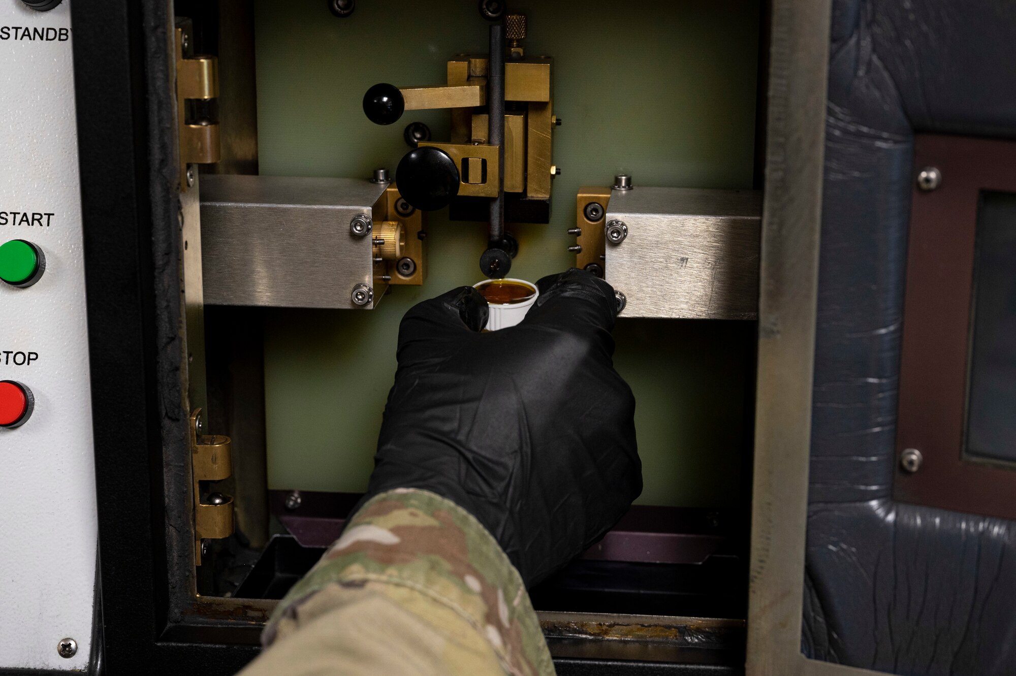 A hand with a black glove on it removes oil from a machine that can detect foreign objects that may be present in the oil.