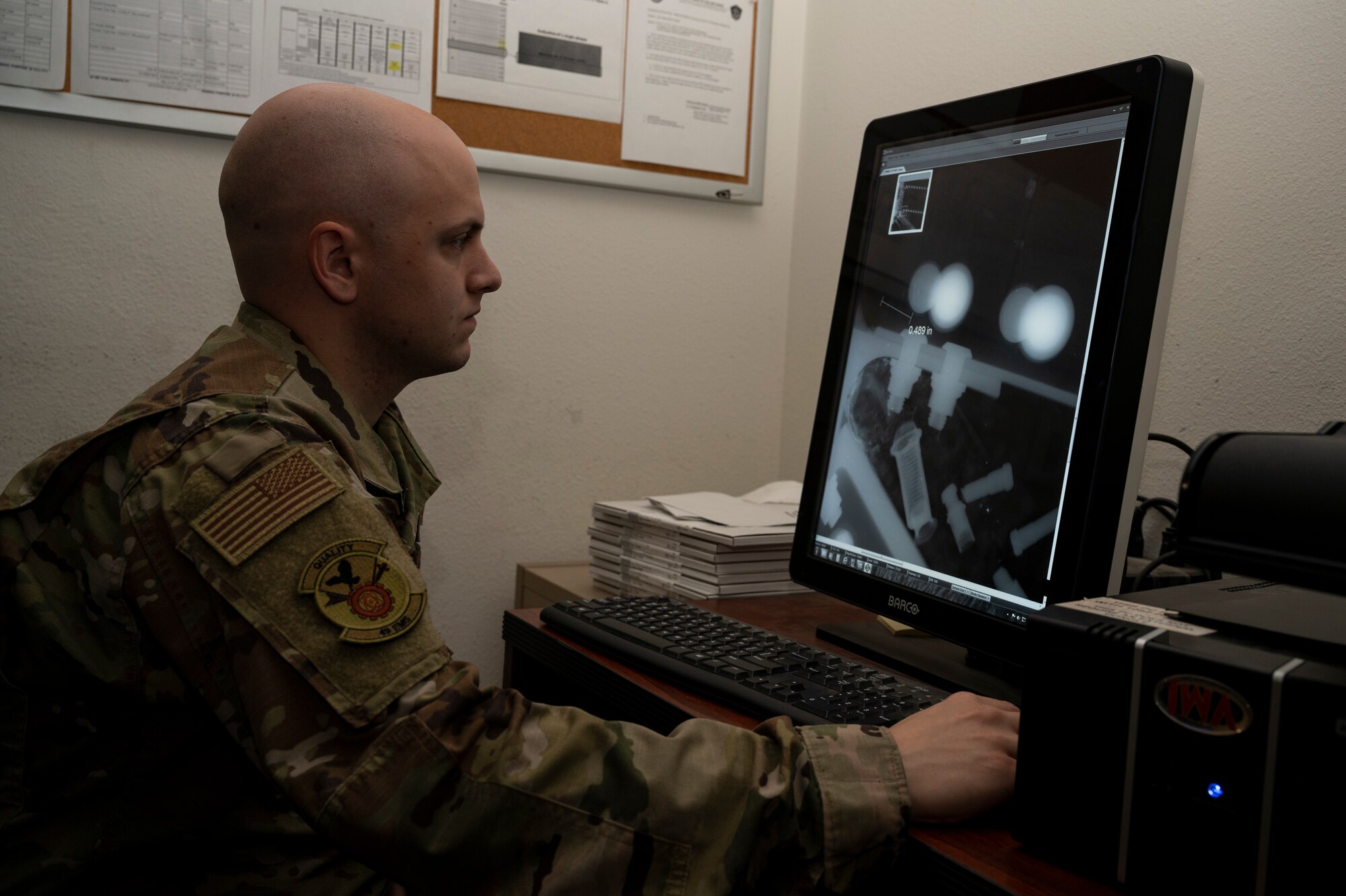 A man in a green OCP uniform analyzes a computer screen that has a x-ray picture of an aircraft part.