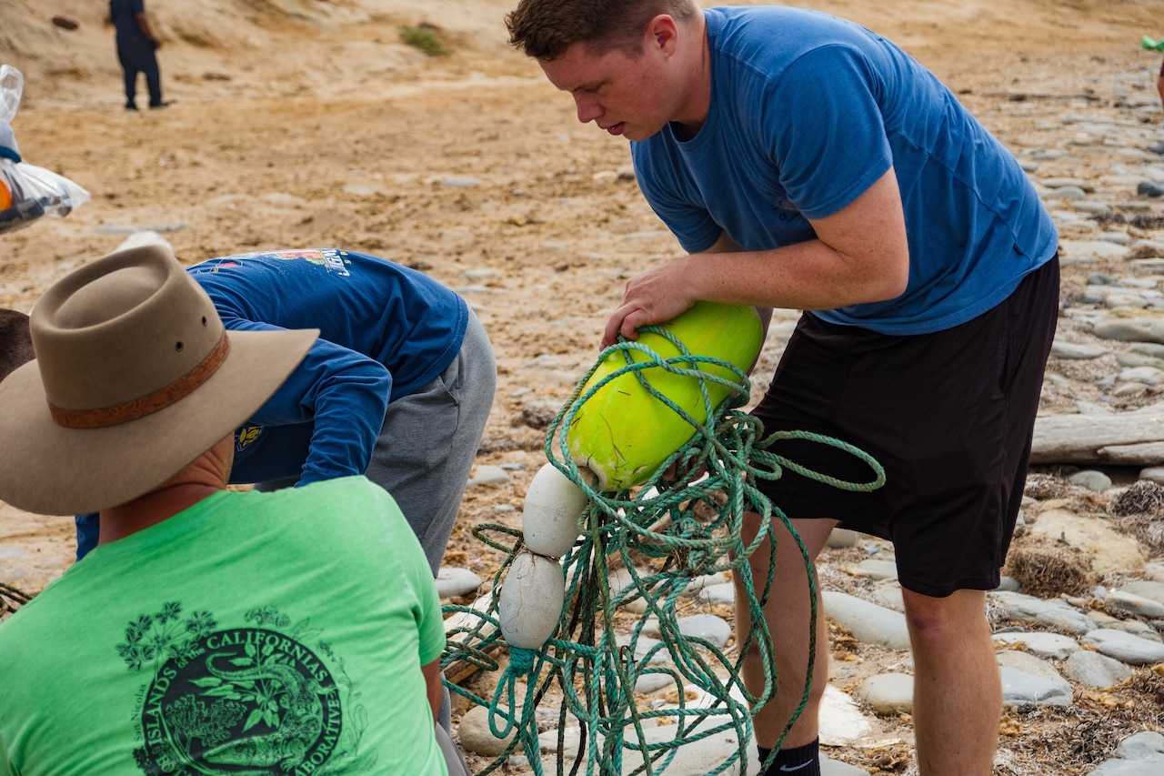 Three people pick up trash on a beach.