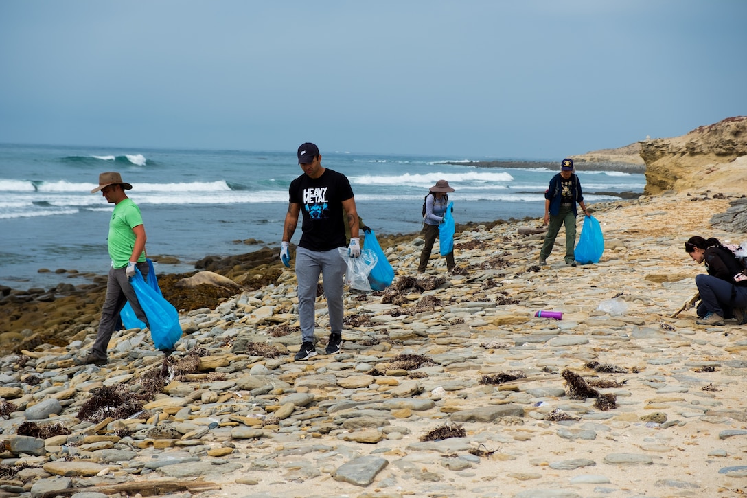A group of people pick up trash on a beach.