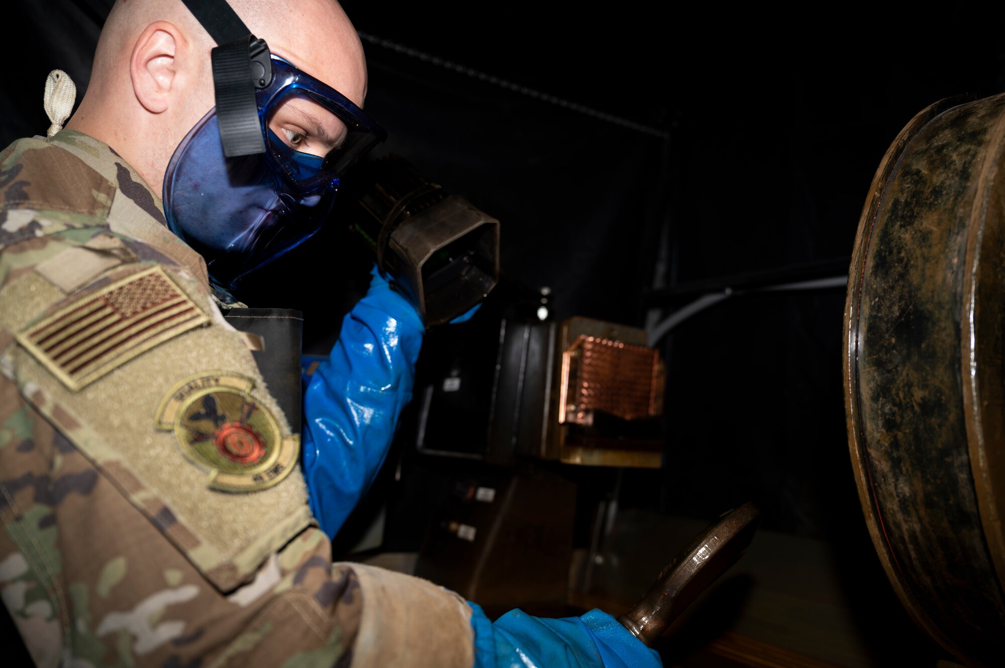 A man in green OCPs points a black light at a piece of an aircraft.