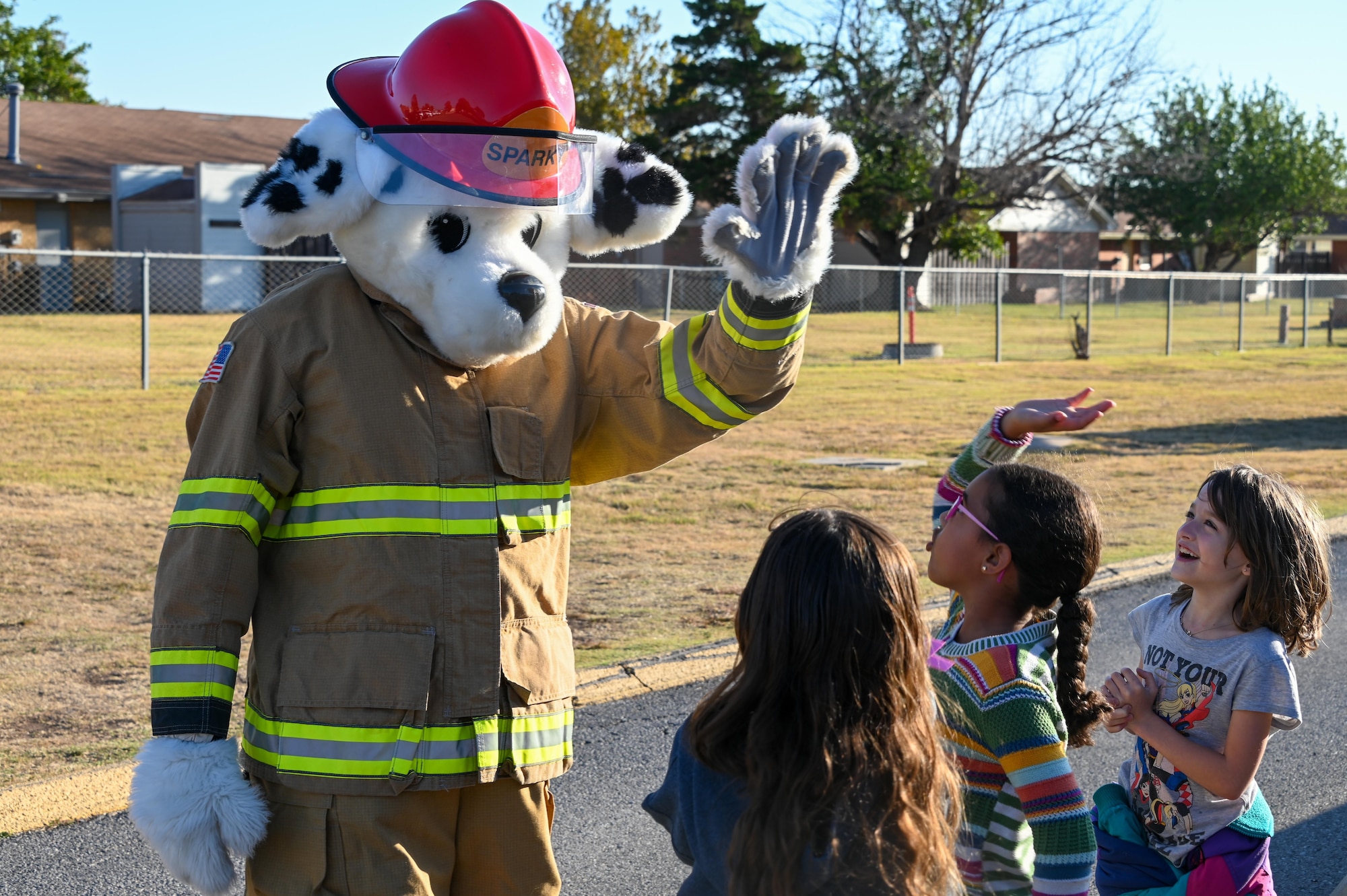 Sparky, 97th Civil Engineer Squadron fire safety mascot, gives a high-five to L. Mendel Rivers Elementary students at Altus Air Force Base, Oklahoma, Oct. 12, 2022. Sparky, the dog, is a mascot created in 1951 to help spread fire safety awareness to children. (U.S. Air Force photo by Senior Airman Kayla Christenson)