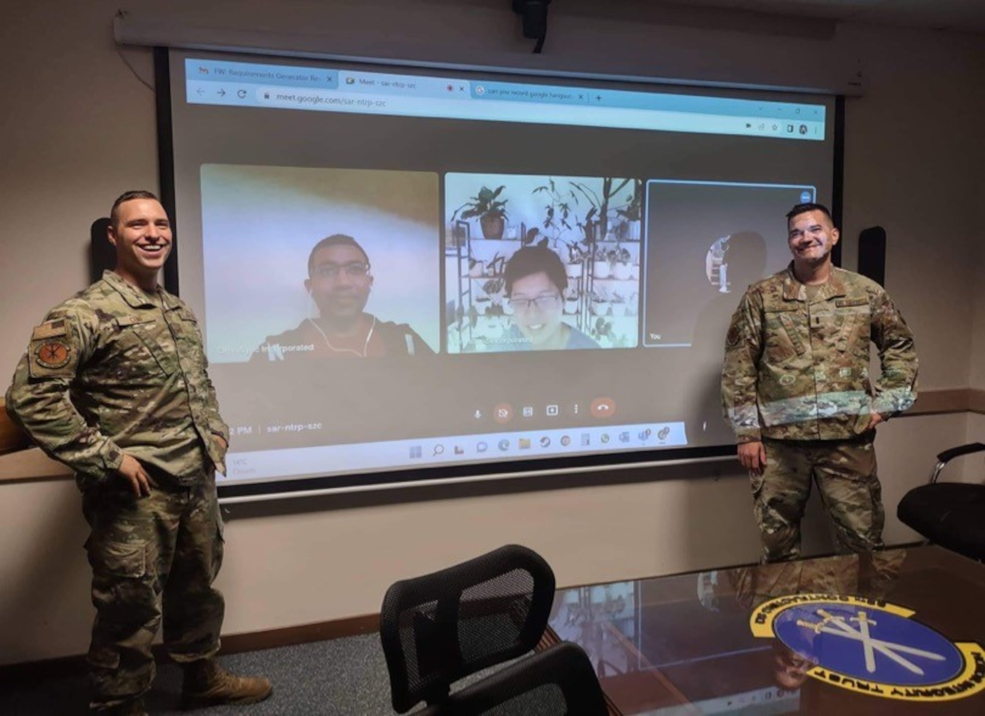 Two Airmen stand in front of a screen