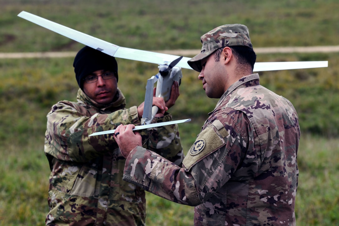 Two service members hold and inspect a small drone while standing in a field.