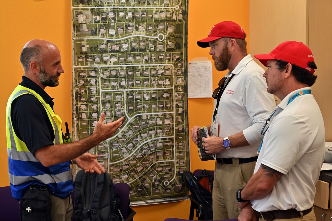 Three men talk near a large map of a residential area.