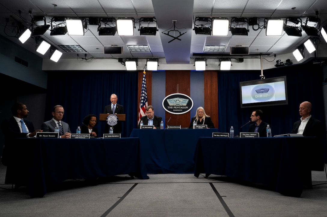 Seven people sit at tables. Another is standing behind a lectern.