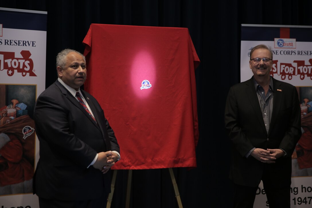 The Secretary of the Navy, the Honorable Carlos Del Toro, left, and artist Charles Fazzino prepare to unveil Fazzino’s donated three-dimensional art piece during a celebration of the 75th anniversary of the Toys for Tots program at Marine Barracks Washington in Washington, D.C., June 3, 2022. Toys for Tots aims to provide happiness and hope to disadvantaged children through the gift of a new toy during the Christmas holiday season. The toys, books, and other gifts collected and distributed by Reserve Marines and the Toys for Tots Foundation offers these children recognition and a positive memory that can last a lifetime. (U.S. Marine Corps photo by Lance Cpl. Briana Vera/Released)