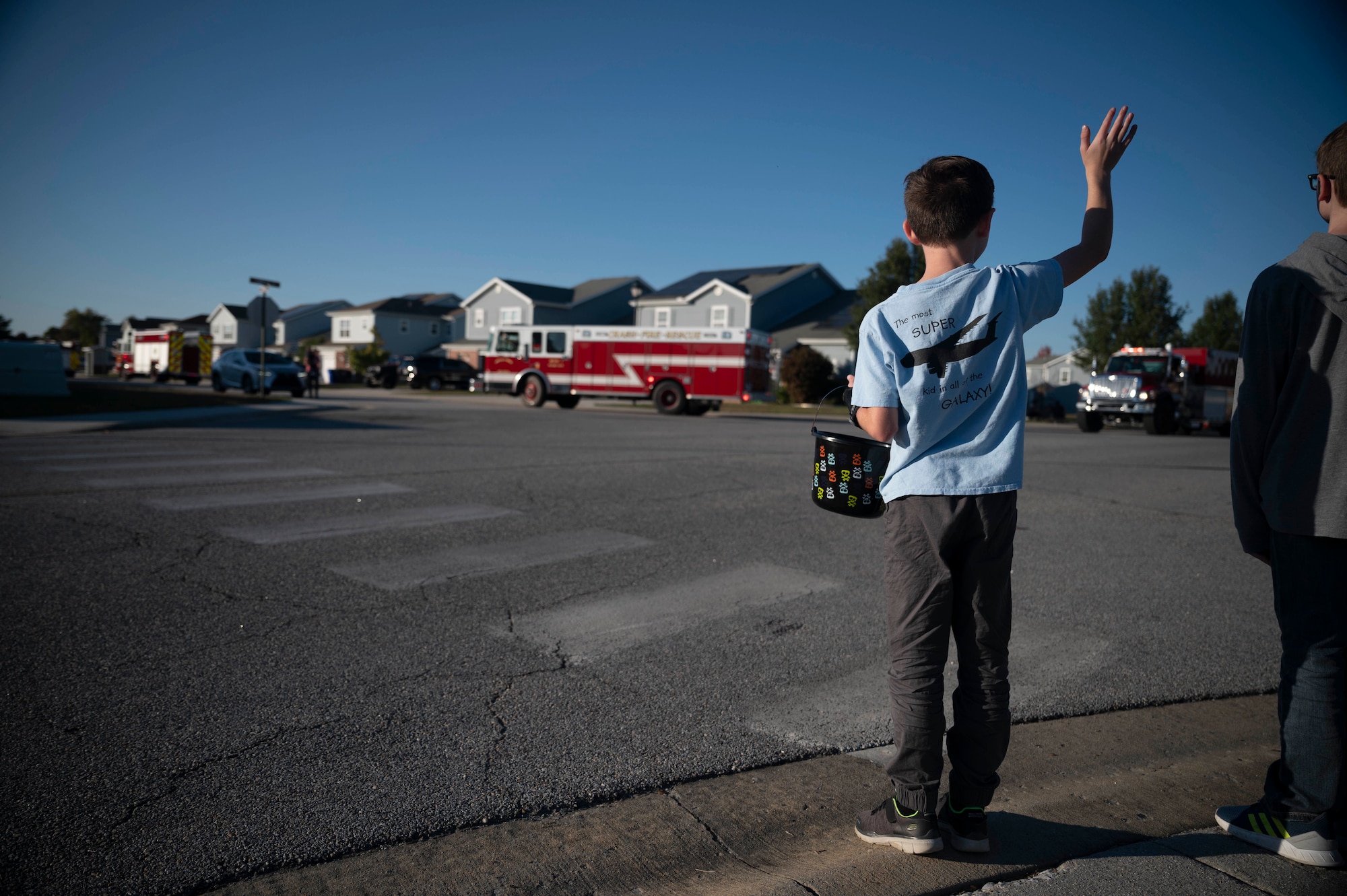 A Team Dover child waves at 436th Civil Engineer Squadron Airmen driving by in an emergency service vehicle during the 2022 Fire Prevention Week parade at Dover Air Force Base, Delaware, Oct. 14, 2022. Dover AFB fire and emergency services drove through base housing to spread awareness on fire prevention week to base housing residents and their families. (U.S. Air Force photo by Staff Sgt. Marco A. Gomez)