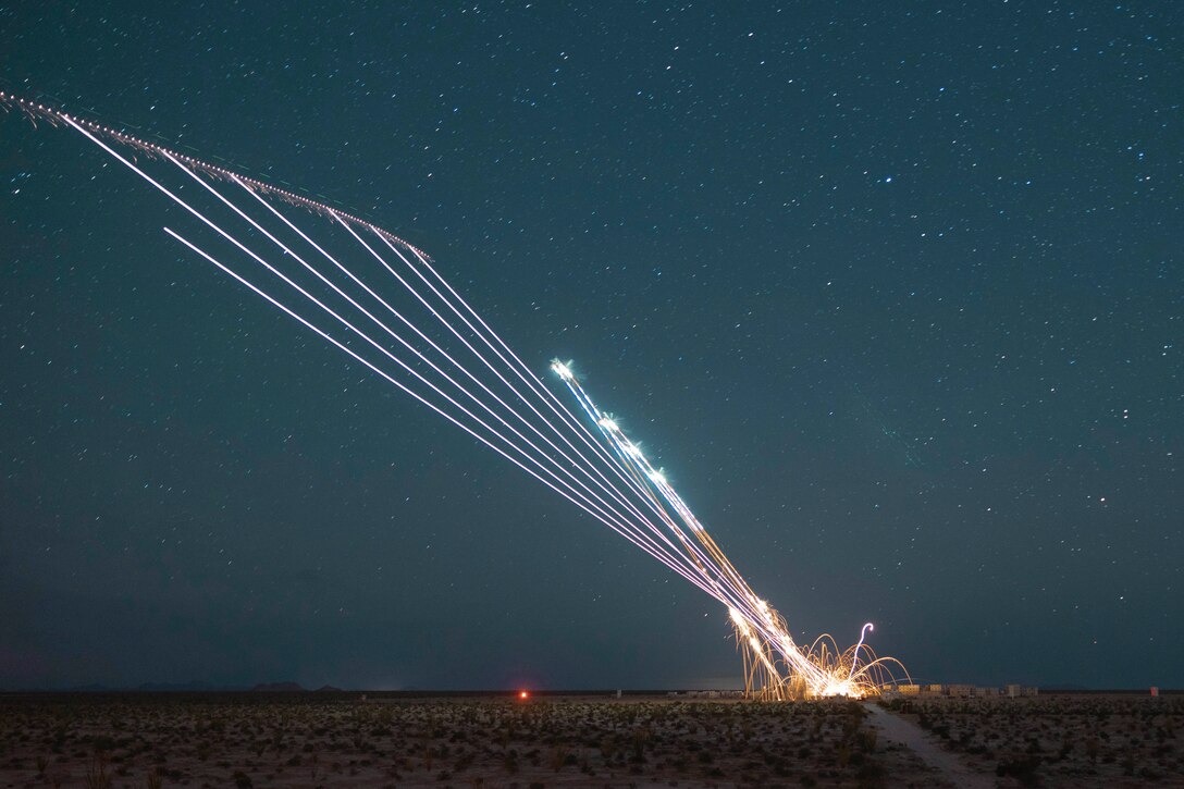 A helicopter fires flares at a desert-like area under a starry sky.