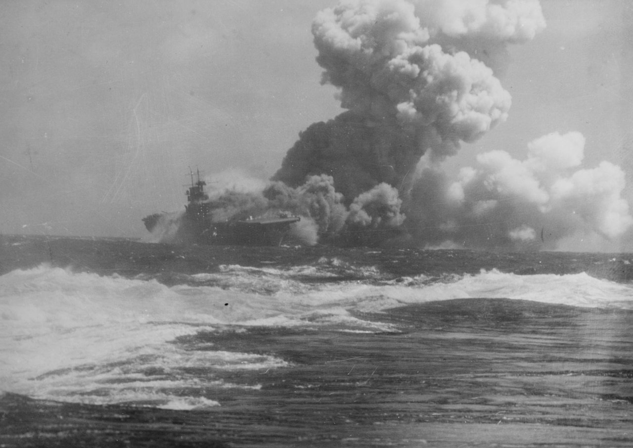 Large plumes of smoke rise from a sinking ship in the ocean.