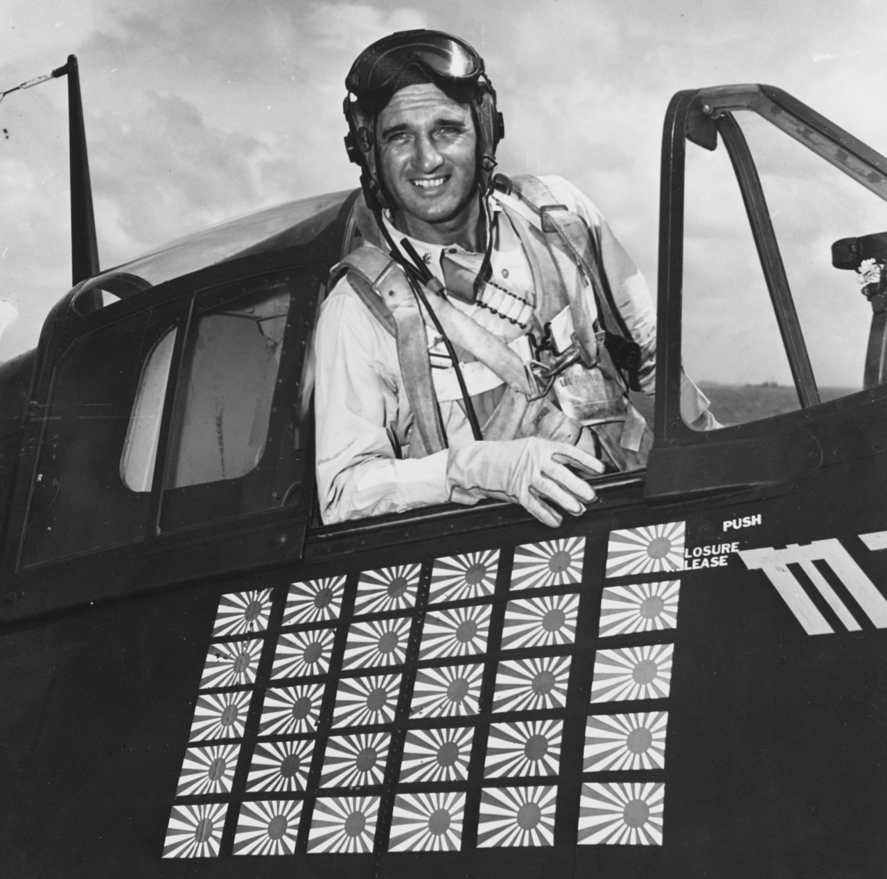 A man sits in the open cockpit of an airplane. Thirty Japanese flags are pasted to the aircraft.
