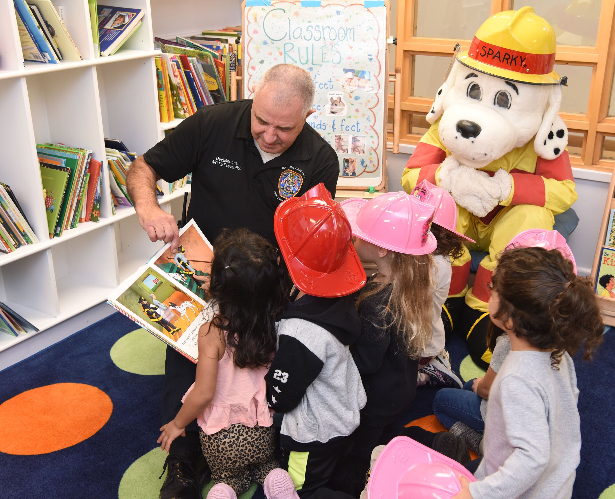 Dave Bootman, 100th Civil Engineer Squadron fire prevention assistant chief, reads a story to pre-school children Royal Air Force Mildenhall, England, Oct. 12, 2022. Sparky the Fire Dog and his firefighter friends visited the child development center as part of Fire Prevention Week events. This year’s FPW theme is “Fire won’t wait: Plan your escape.” Other activities included information booths, open house at the fire department, bowling and a fire muster. (U.S. Air Force photo by Karen Abeyasekere)