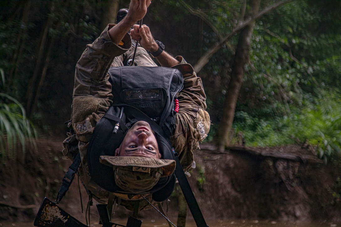 A soldier hangs upside down on rope in a jungle.