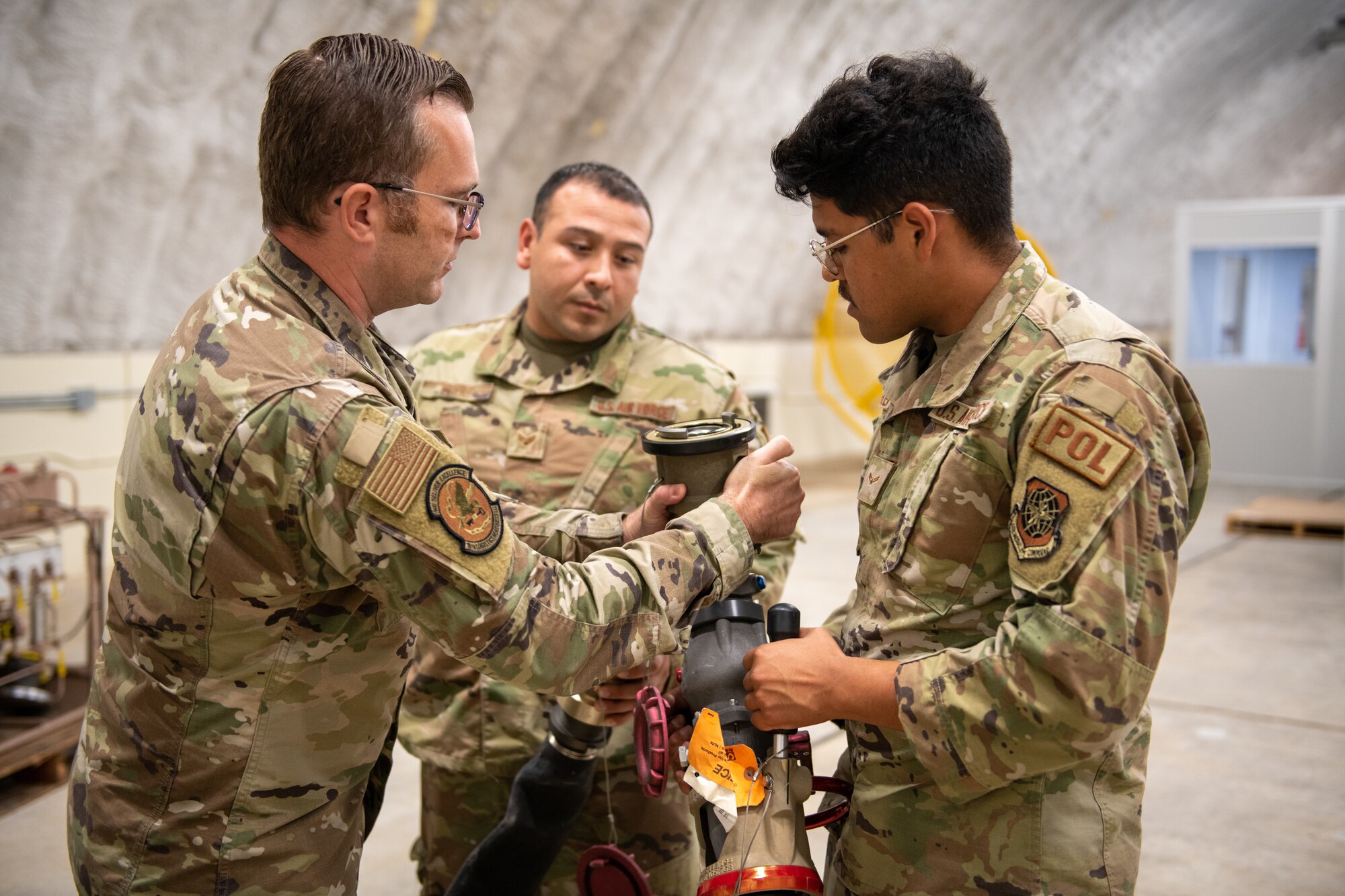 Master Sgt. Matt Yunker, 18th Logisitics Readiness Squadron chief of fuels operations, shows Senior Airman Felix Cruz and Airman 1st Class Ivan Herrera, 22nd LRS fuels distribution operators, how the Versatile Integrating Partner Equipment Refueling Kit would connect to a fuel hose during a hot pit refueling mission Oct. 13, 2022, at Kadena Air Base, Japan.