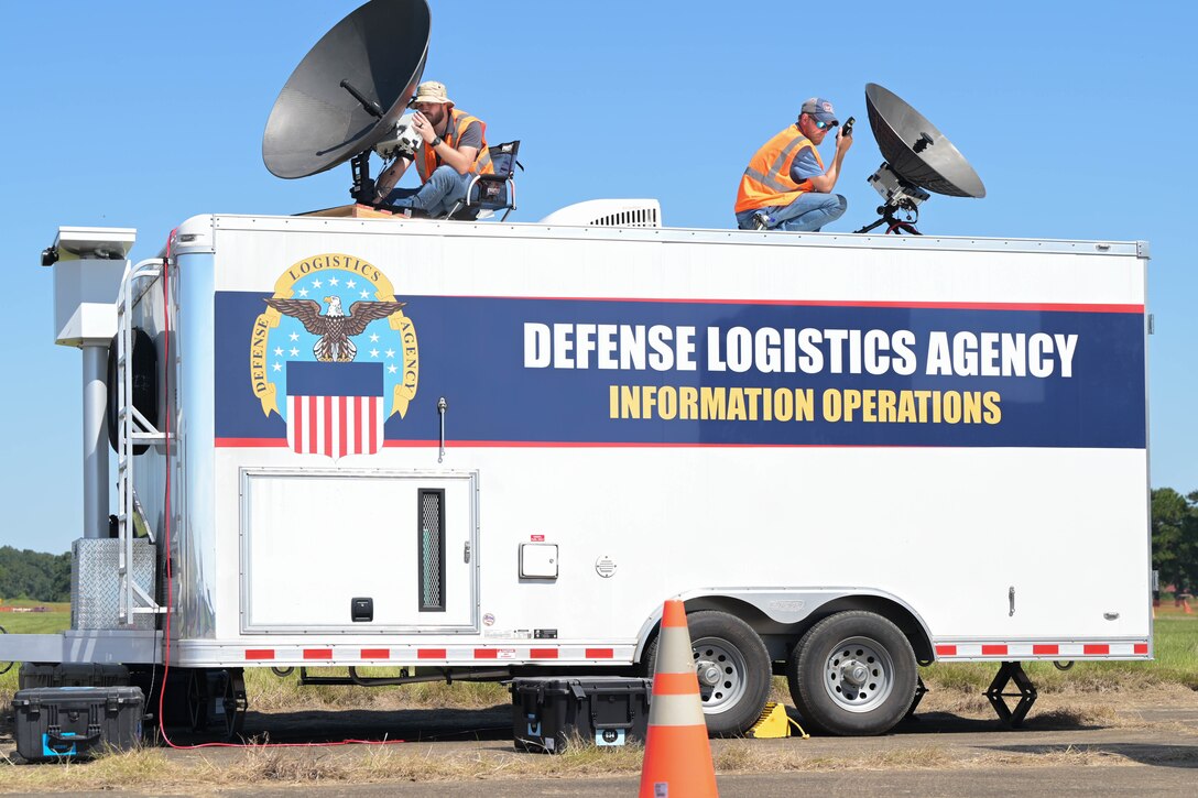 Two men set up satellites on an emergency response trailer.