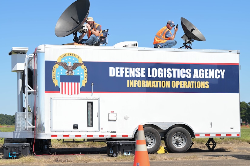 Two men set up satellites on an emergency response trailer.