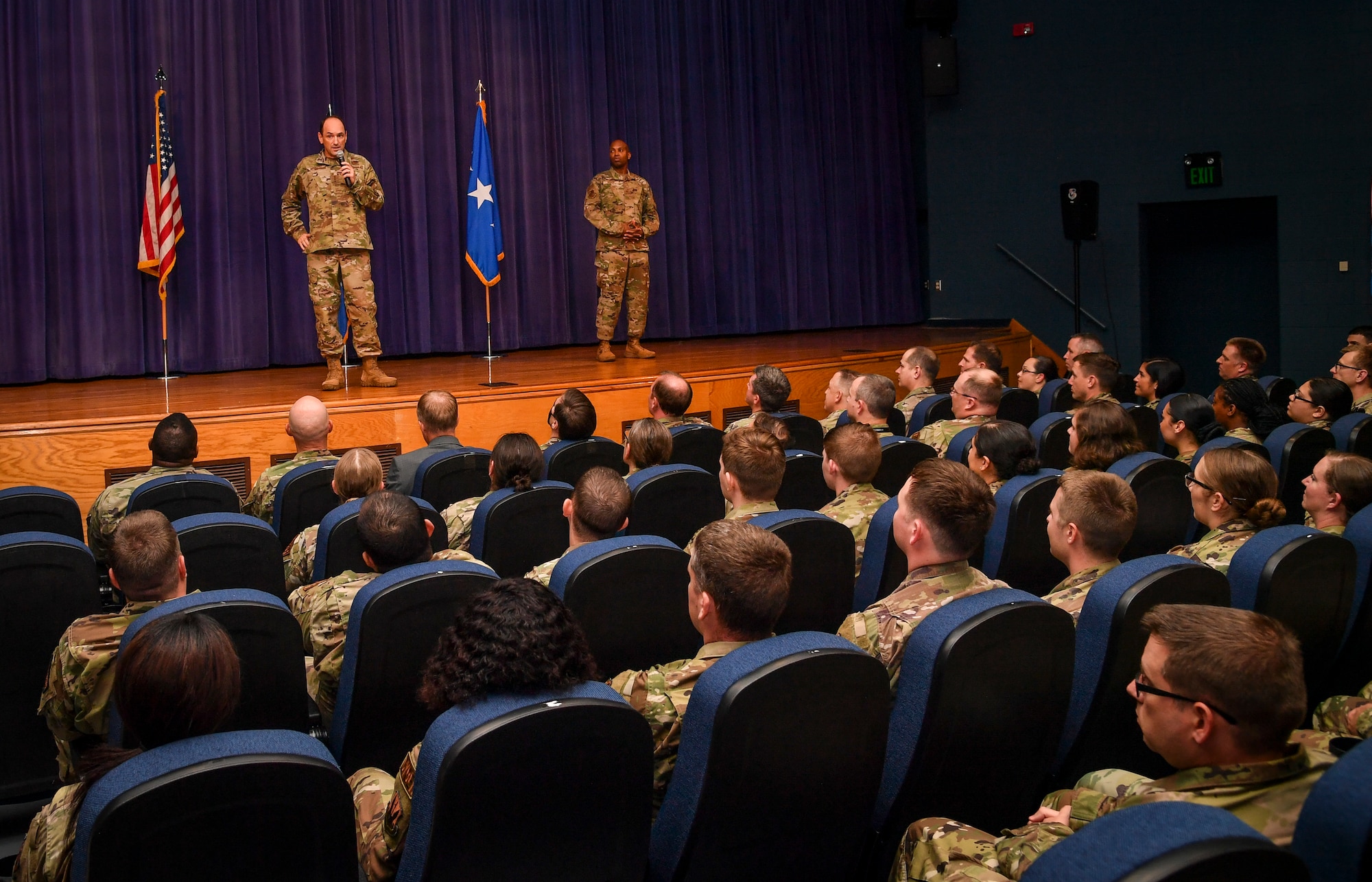 Two individuals stand on stage and talk to folks.