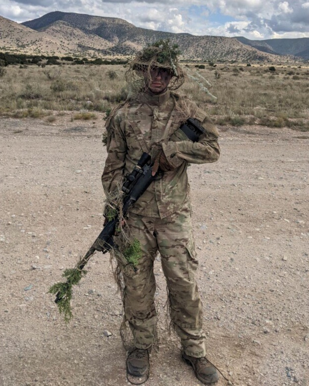 A man in uniform outdoors holds a rifle.