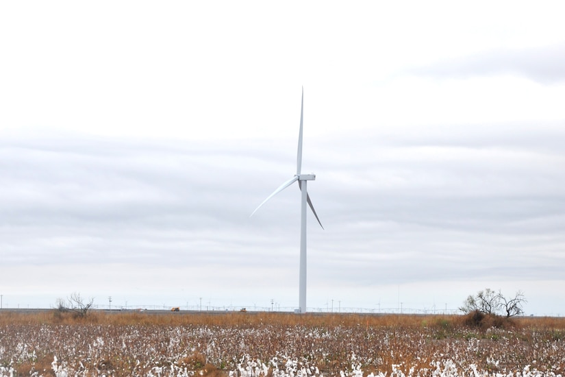 A wind turbine extends high above a scrubby landscape.