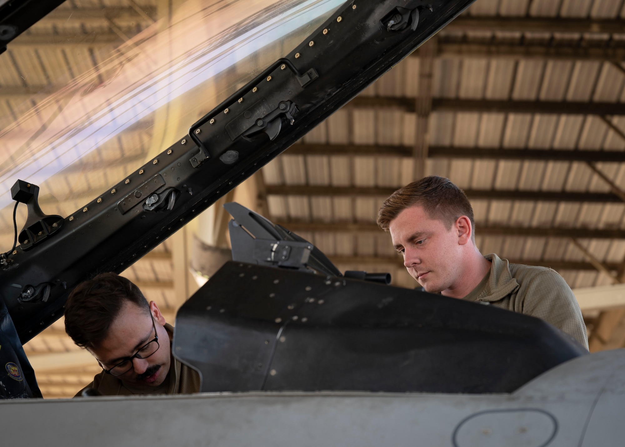 Two airmen perform maintenance on a cockpit of a F-16